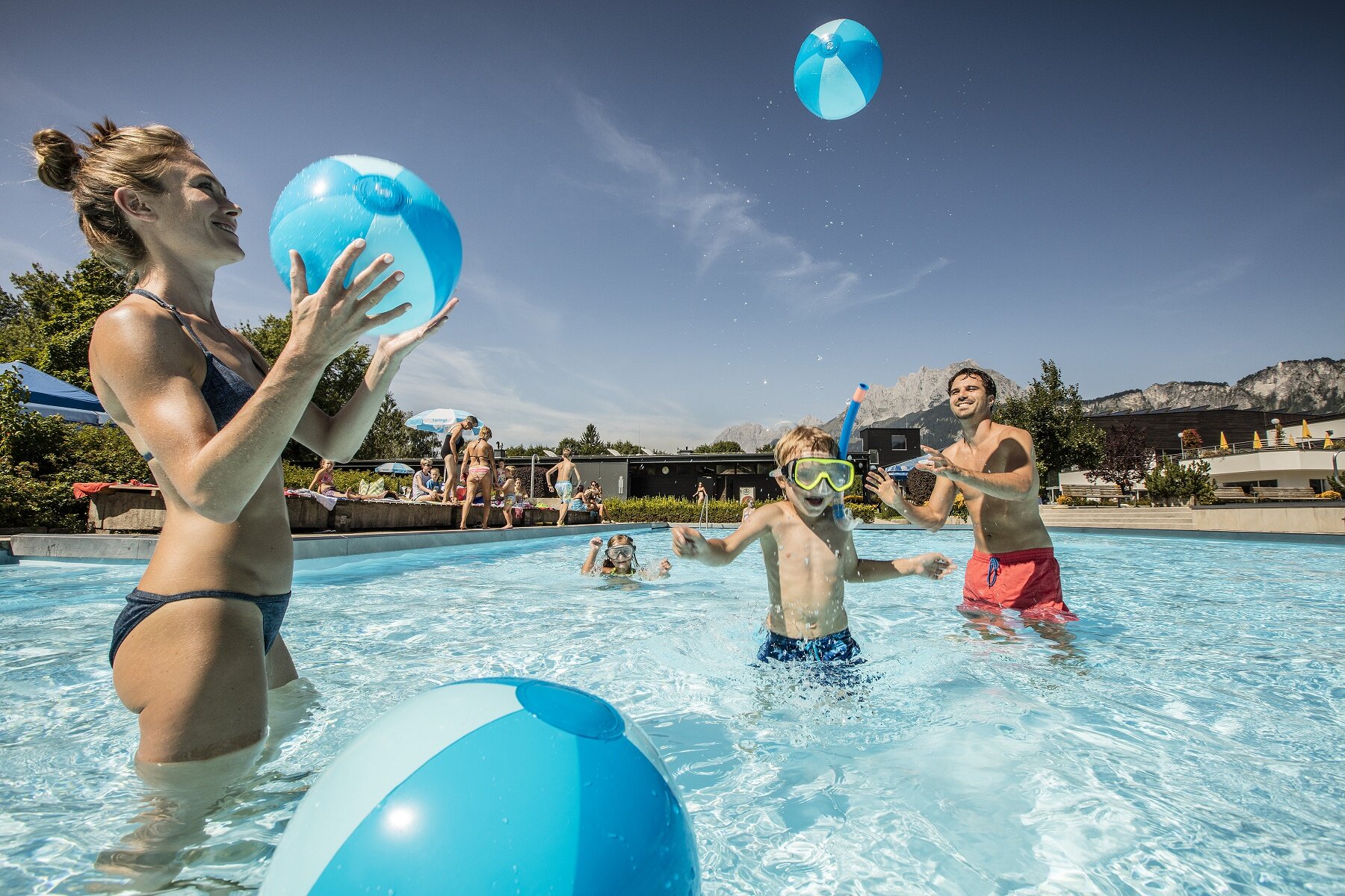 Familie spielt Ball im Freibad der Panorama Badewelt, im Hintergrund der Wilde Kaiser